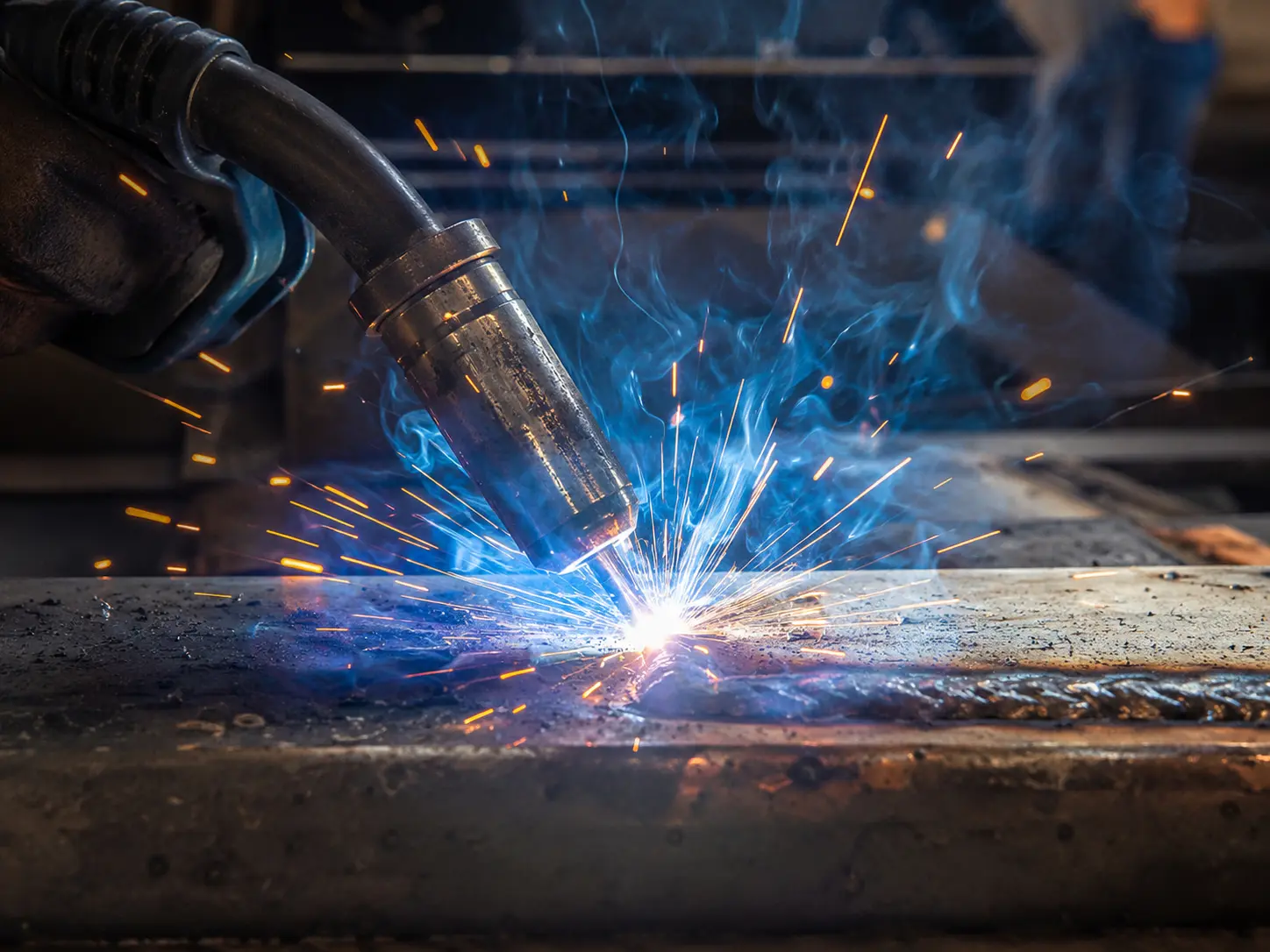 MIG welding torch joining steel as sparks and smoke rise
