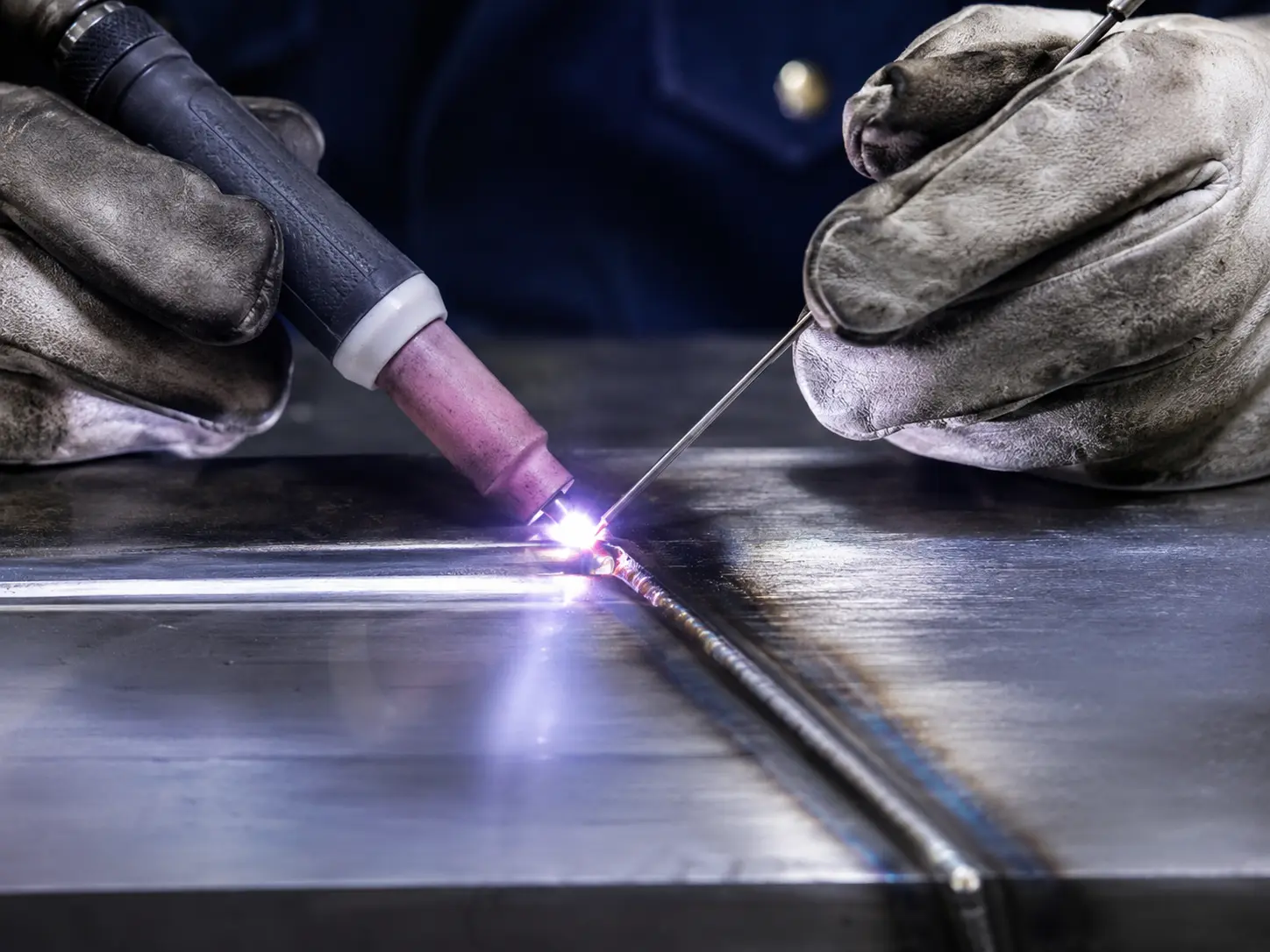 Gloved hands TIG welding a clean seam in sheet metal